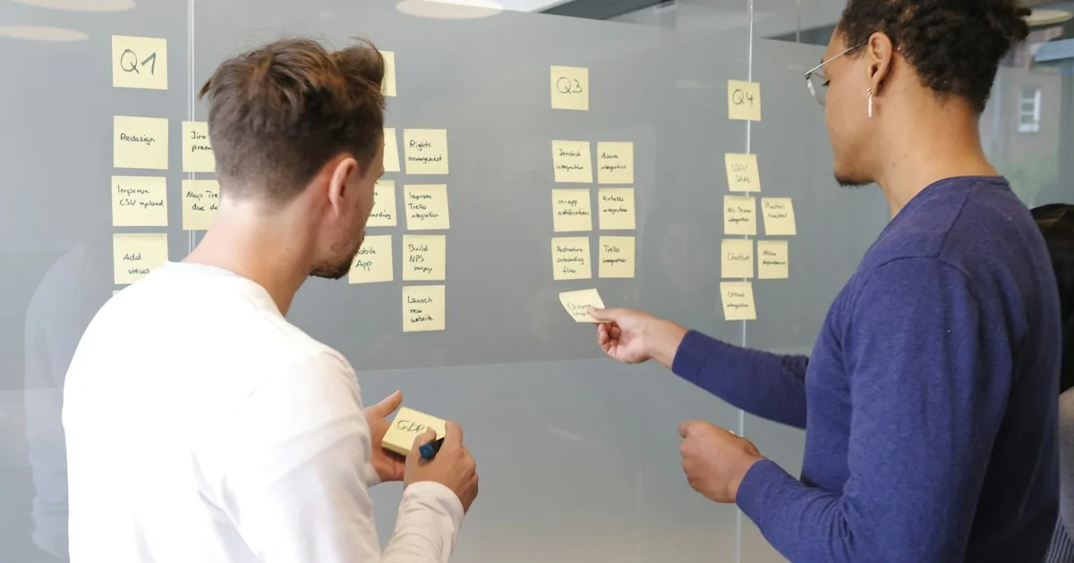 Two colleagues planning work with yellow sticky notes on a glass wall.