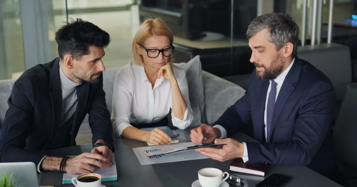 Three professionals discussing work at a table with a laptop.