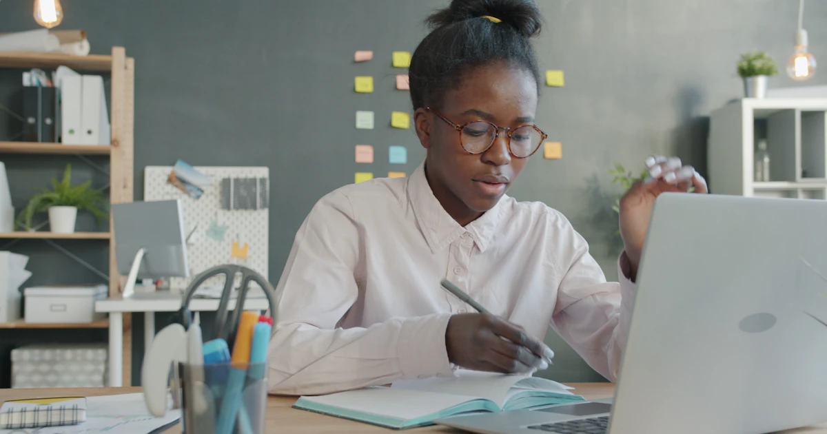 A professional reviewing work at a desk with a laptop and notebook.